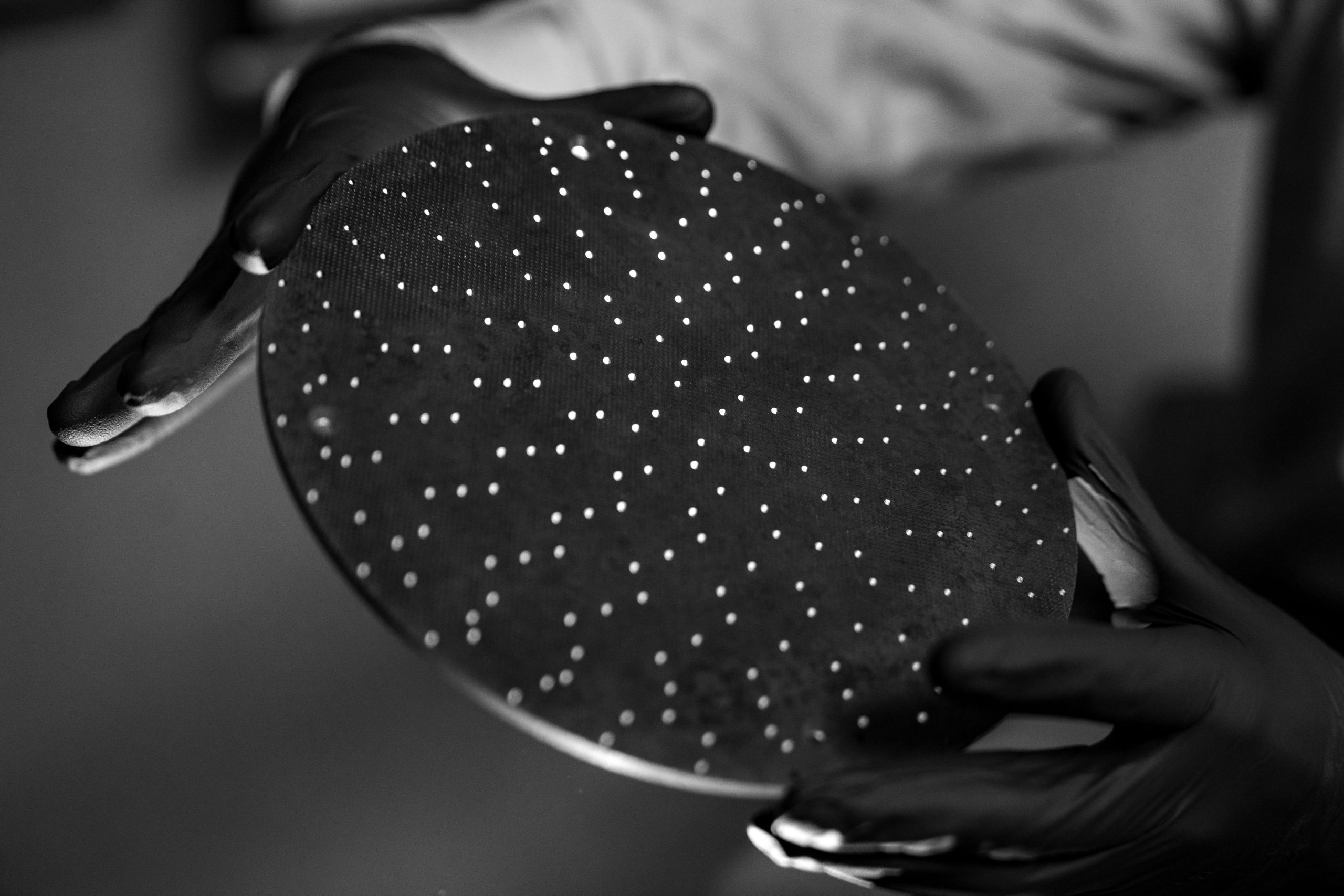 hands delicately holding a solid, disk-shaped part with a grid of holes that Bullen Ultrasonics created using CNC machining.